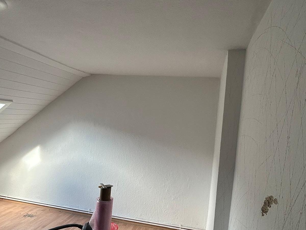 Dachgeschosszimmer mit gestrichener Wand und Decke, Material für die nächsten Schritte im Vordergrund