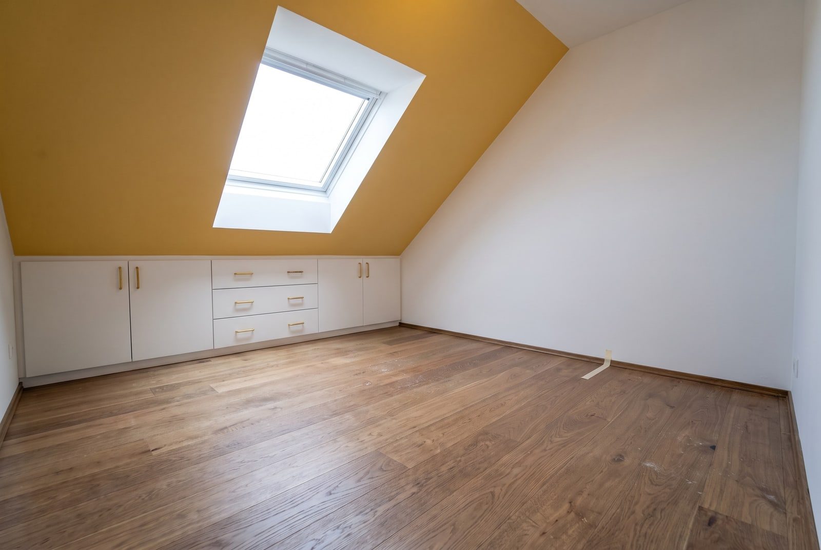 Renoviertes Dachgeschosszimmer mit Dachfenster, ockerfarbener Schräge und weißen Einbauschränken