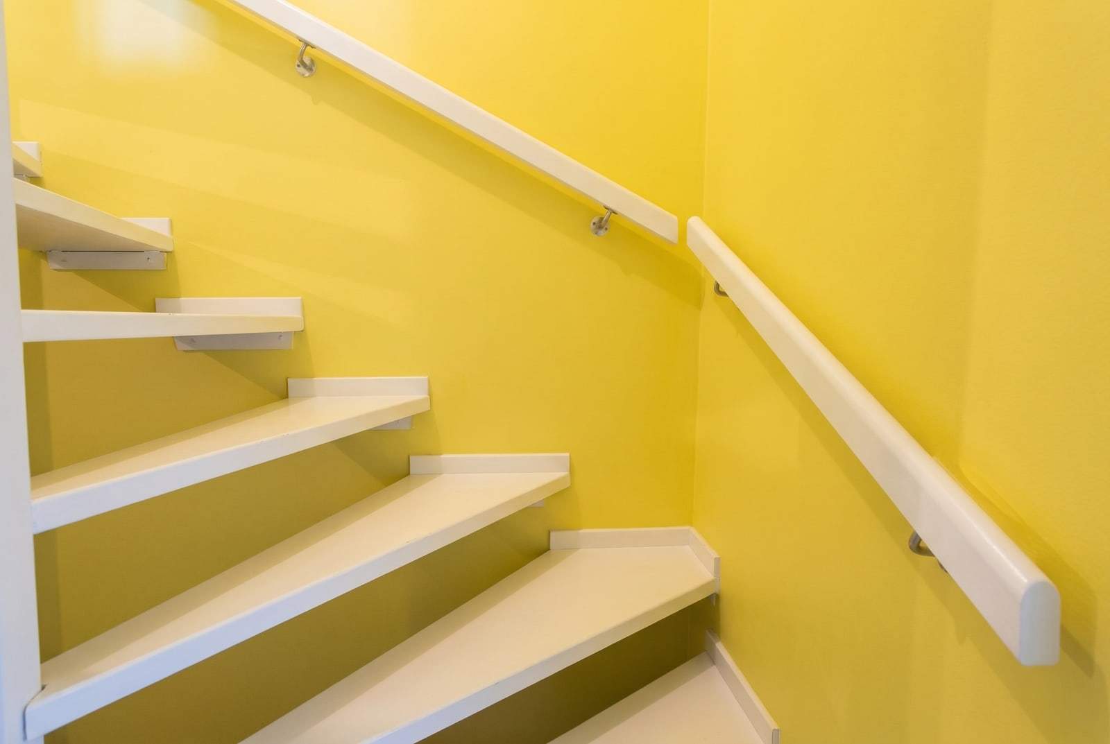 Gewendelte Treppe mit gelb gestrichenen Wänden, weißen Stufen und weißen Wandhandläufen