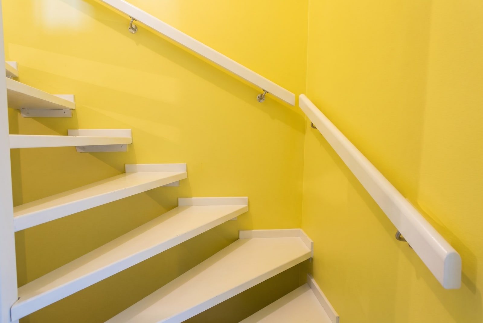Gewendelte Treppe mit gelb gestrichenen Wänden, weißen Stufen und weißen Wandhandläufen