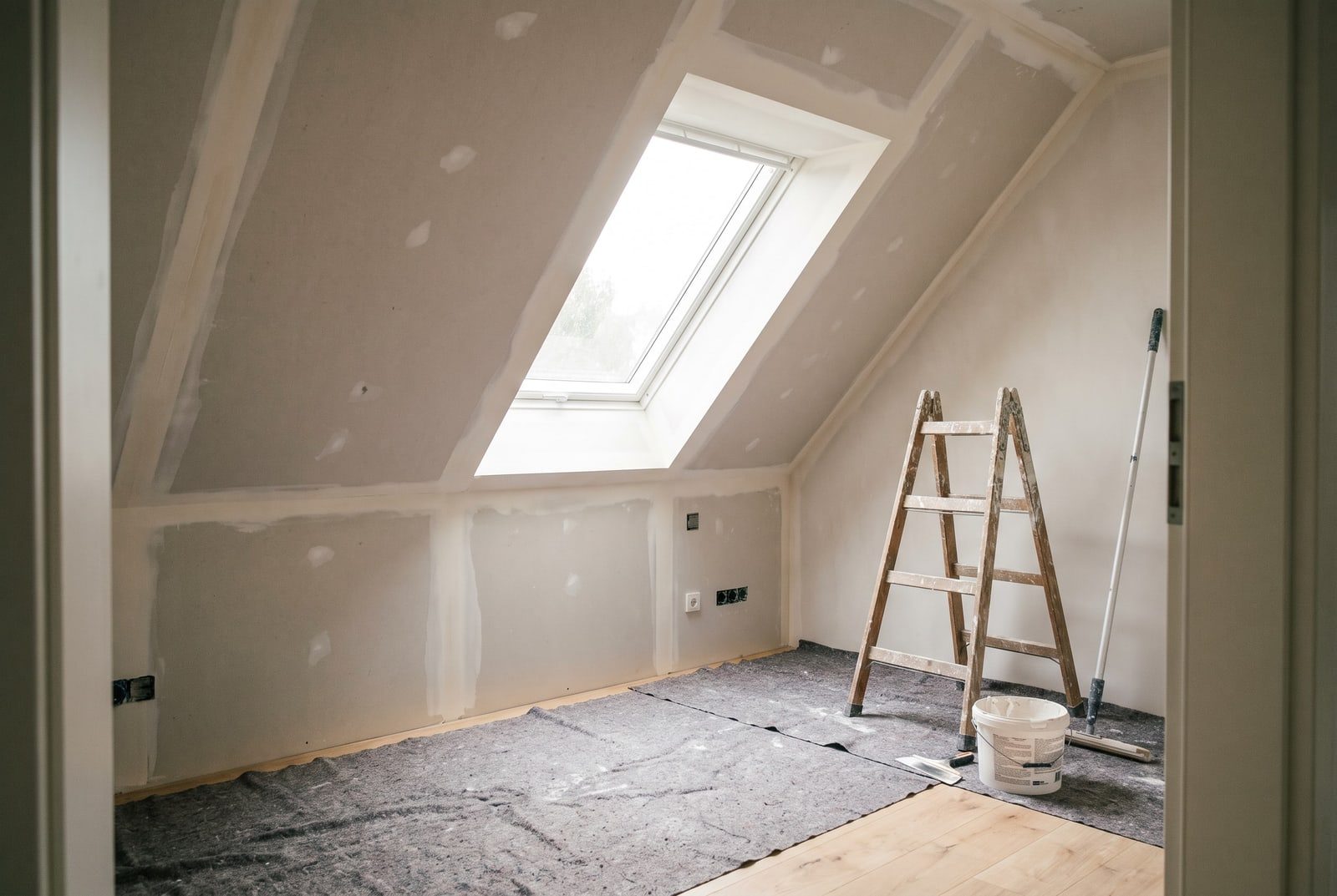 Ausgebautes Dachgeschoss: Dachschrägen und Drempel mit Gipsplatten verkleidet und gespachtelt, Dachfenster, Holzleiter und Spachteleimer