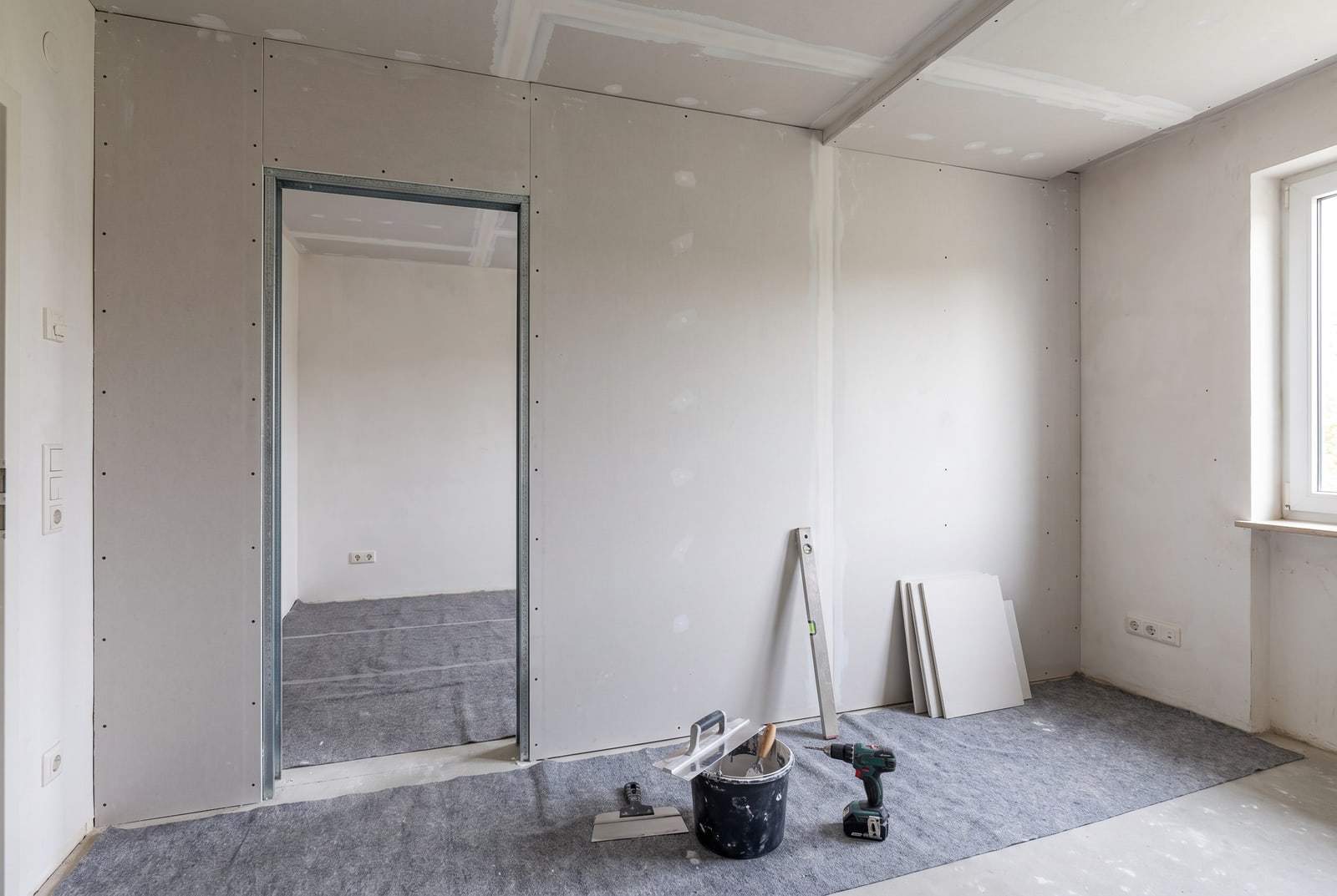 Neu gestellte Trockenbauwand mit Türöffnung und abgehängter Decke, Fugen gespachtelt, Glättkelle, Spachtel und Akkuschrauber auf Malervlies