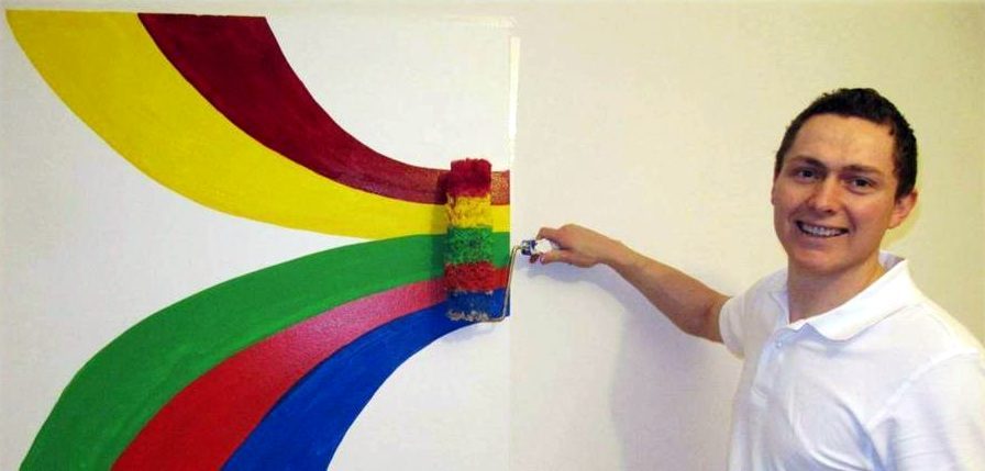 Malermeister Viktor Horn rollt ein farbiges Wandbild in Gelb, Rot, Grün und Blau